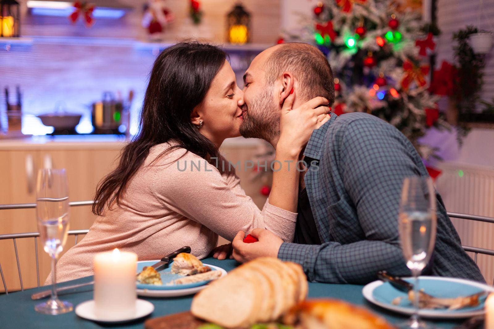 Happy couple kissing in xmas kitchen after marriage proposal enjoying christmas holiday sitting at dinning table. Couple enjoying spending time together during winter season