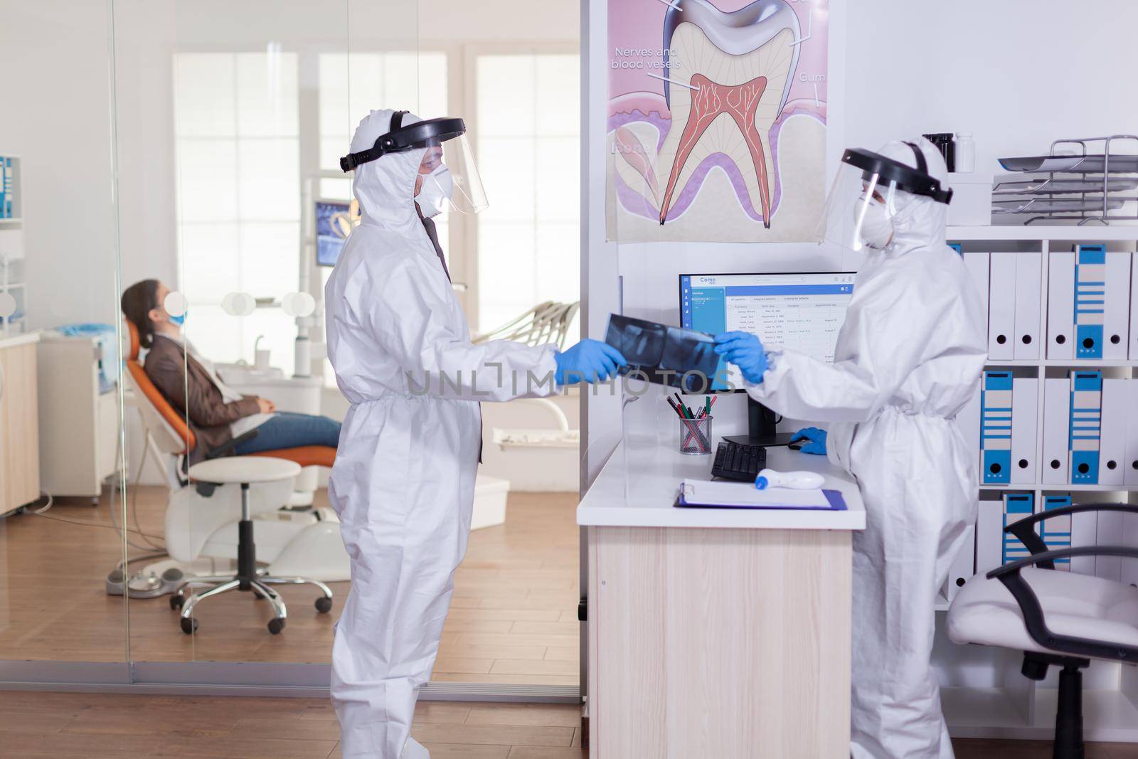 Dental receptionist dressed in coverall giving doctor patient x-ray by DCStudio