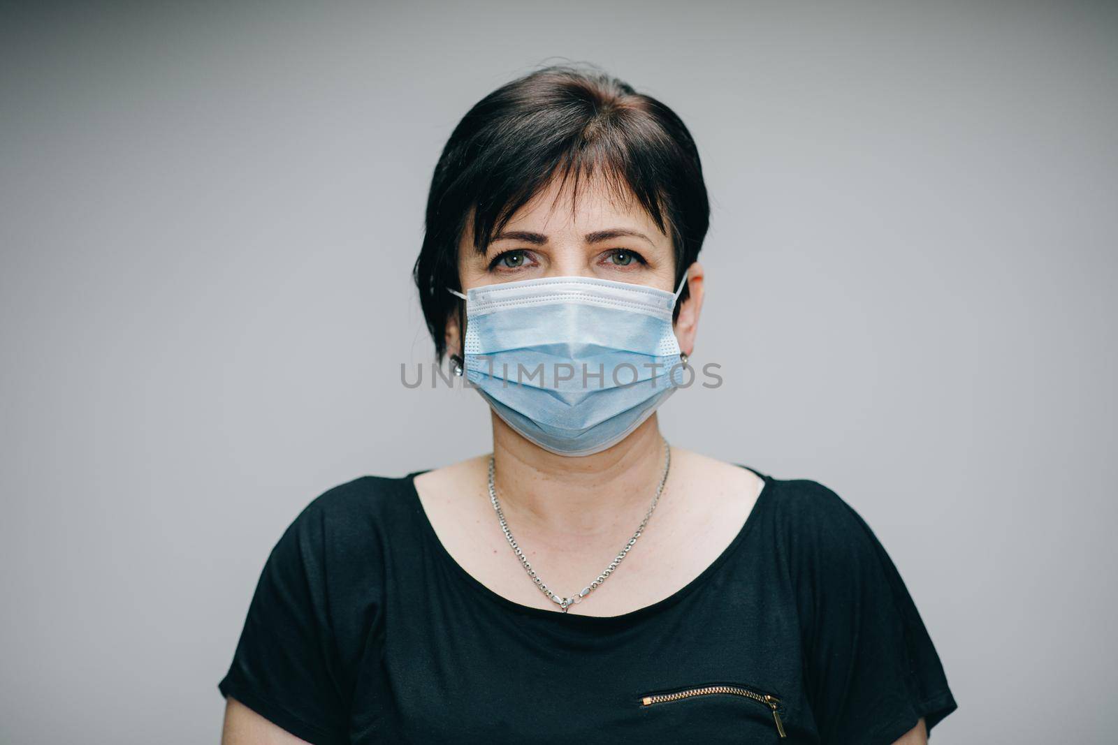 Woman in Medical Mask. Breathes deeply and looking at camera on grey background outdoor. Health care and medical concept. by uflypro