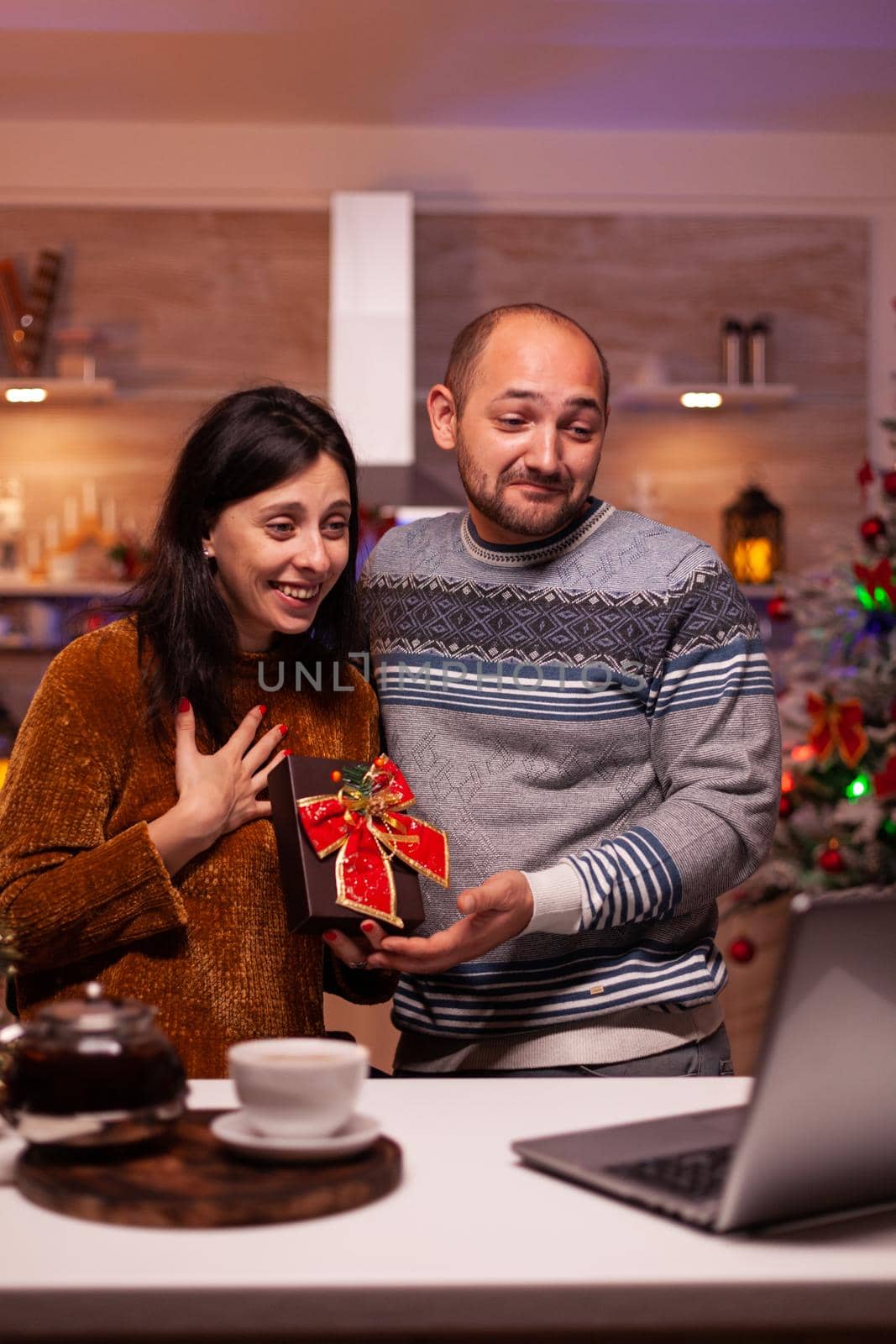 Happy couple showing xmas winter holiday gift to remote friends during online videocall meeting conference enjoying christmas time together. Cheerful family celebrating winter festive season