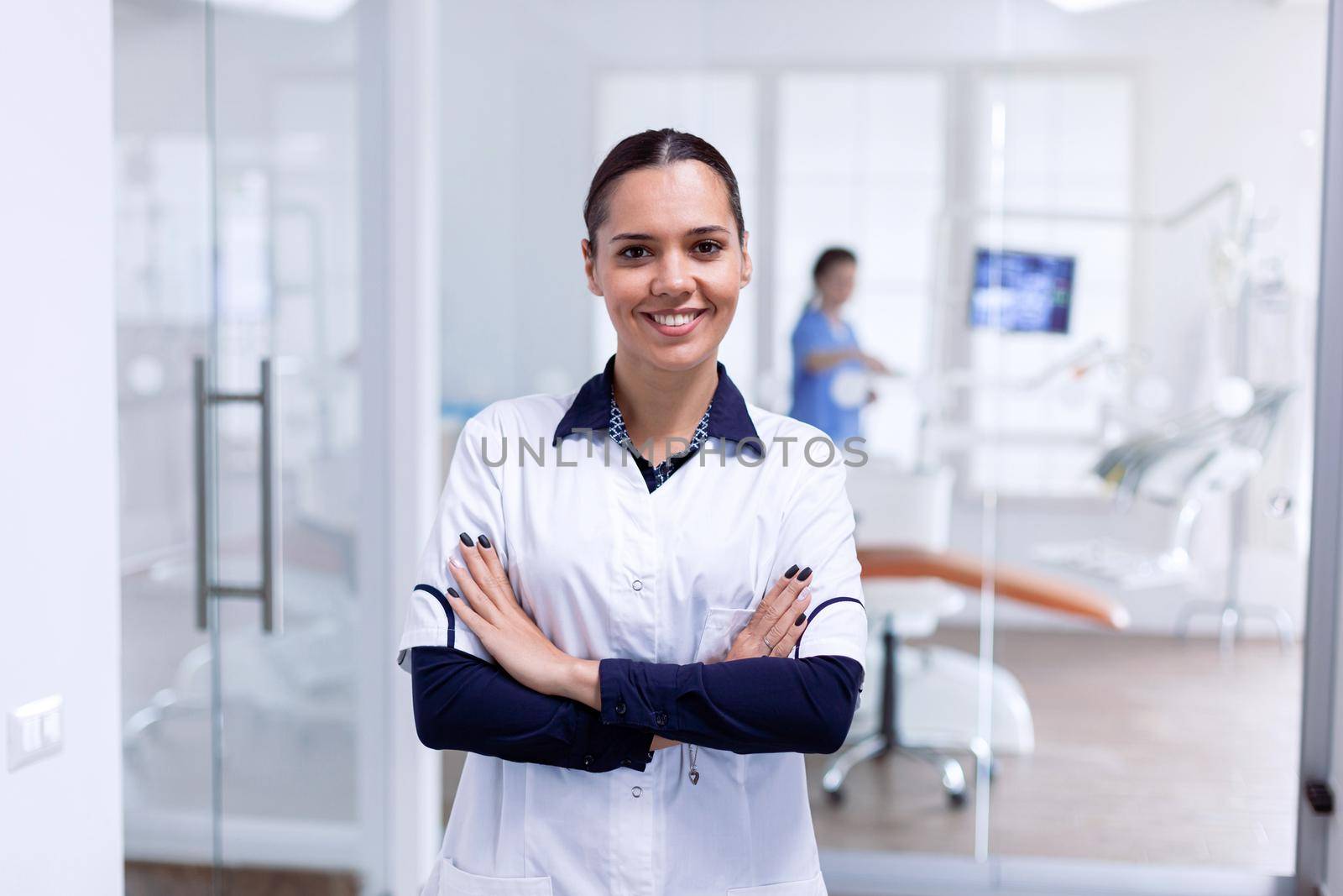 Portrait of stomatology medic in dental reception with arms crossed looking at camera wearing uniform. Happy smiling dentist in her orthodontic office.
