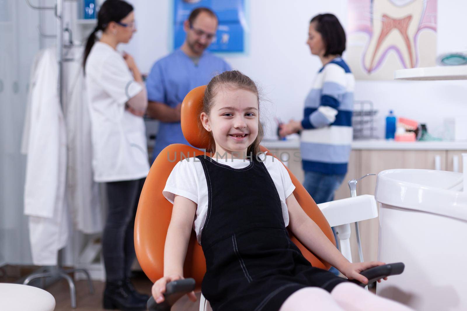 Cheerful kid sitting on chair in dentist office during visit for bad tooth treatment. by DCStudio