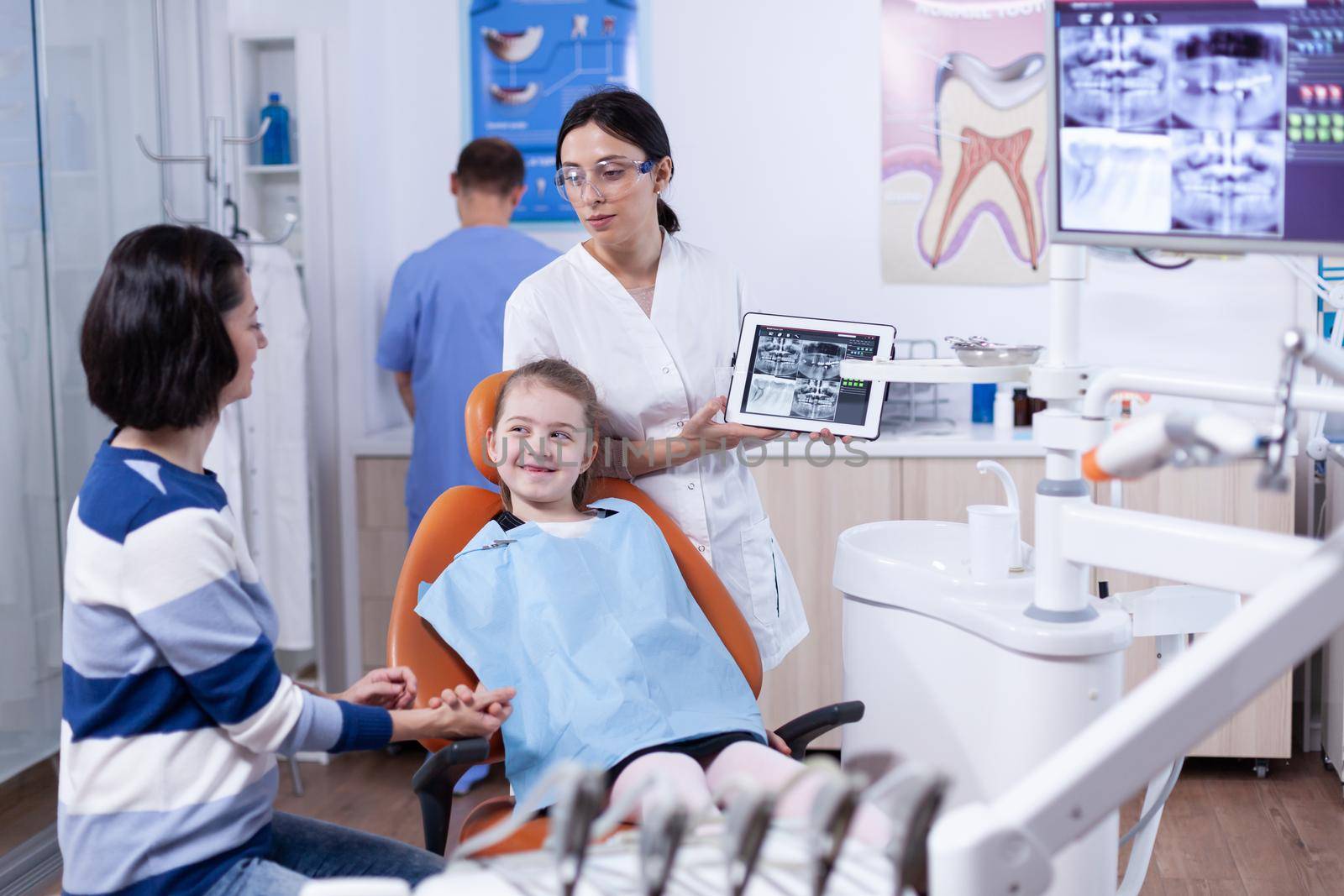 Little girl with missing tooth smiling at parent during dentistiry examining wearing bib by DCStudio