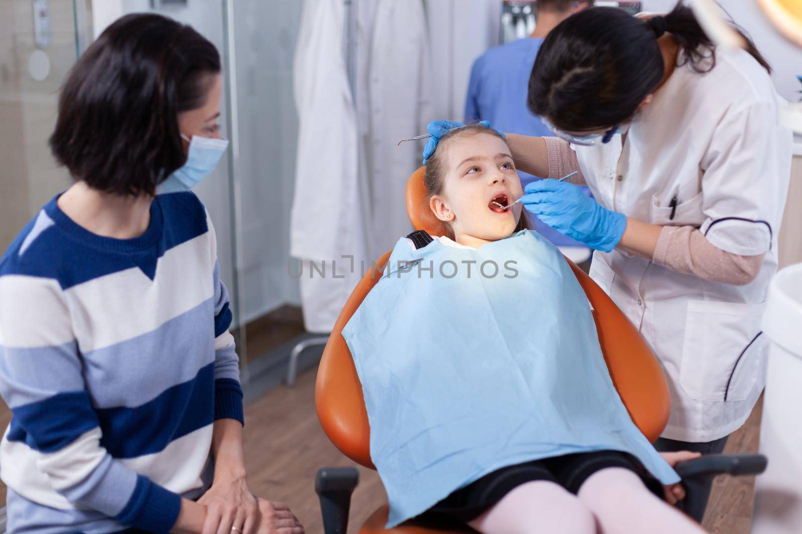 Little girl in the course of dental treatment from young dentist in office. Dentistry specialist during child cavity consultation in stomatology office using modern technology.
