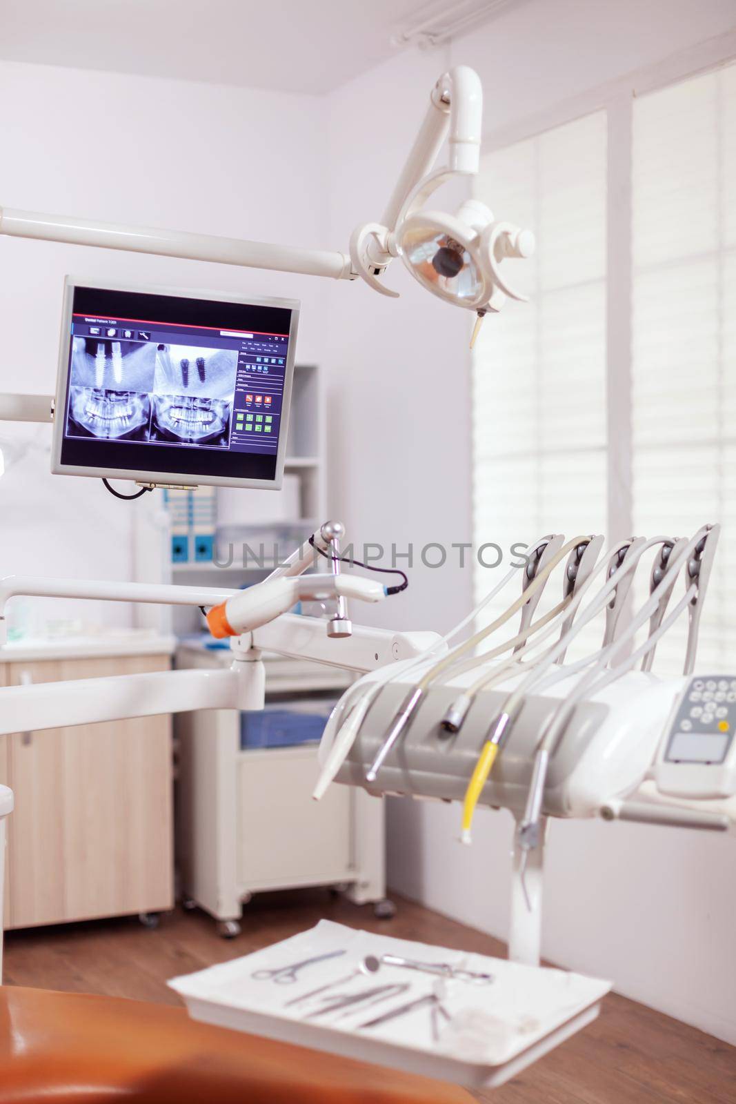 Close-up view of dental tools and professional chair at dentist. Stomatology cabinet with nobody in it and orange equipment for oral treatment.