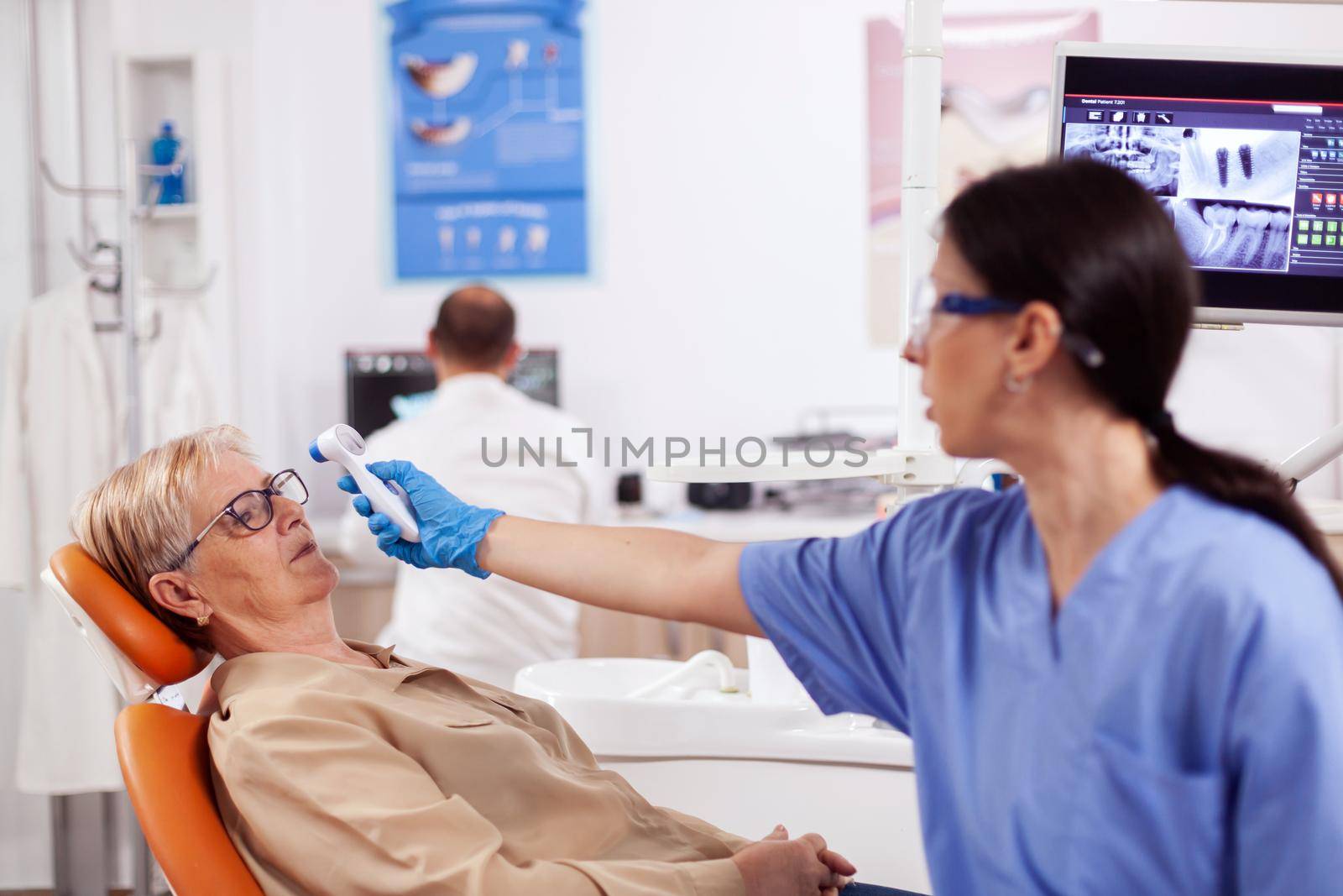 Dentist assistant measuring senior woman body temperature by DCStudio