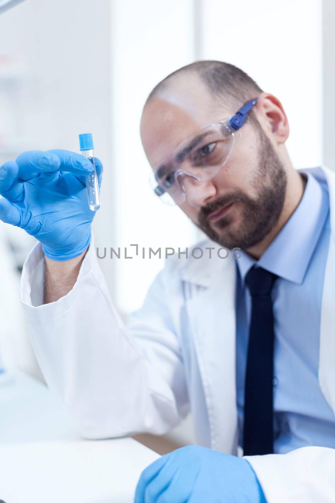 Male scientist with sterile gloves looing at test tube with genetic material. Researcher in biotechnology sterile lab holding analysis in tube wearing gloves and protection glasses.