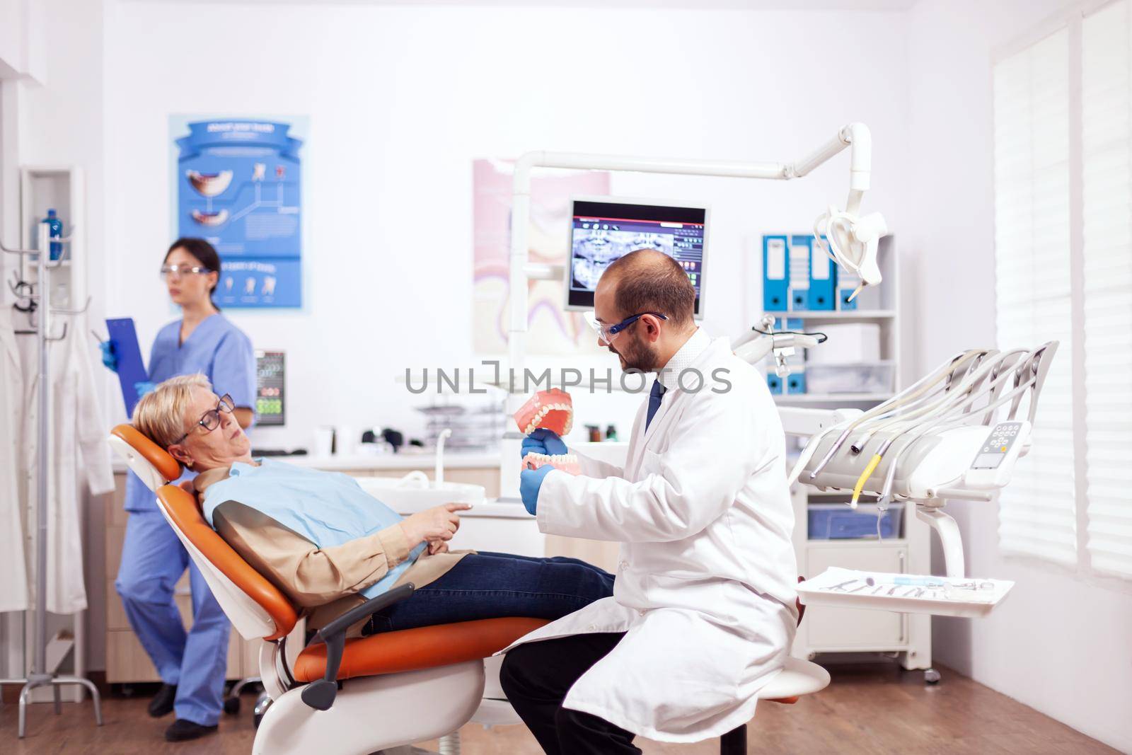 Senior woman at dentist check up in modern private stomatological clinic. Medical teeth care taker discussing with senior woman about mouth hygiene.