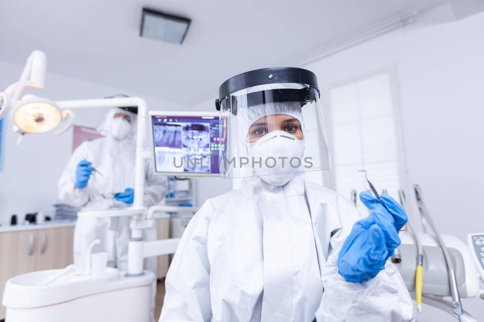 Patient pov of dentist holding tool for teeth treatment in dental office. Stomatolog wearing safety gear against coronavirus during heatlhcare check of patient.