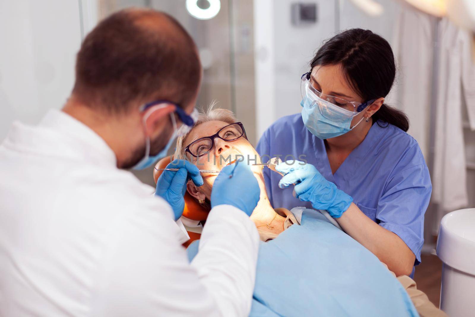 Nurse helping stomatolog during teeth treatment of senior woman. Elderly patient during medical examination with dentist in dental office with orange equipment.