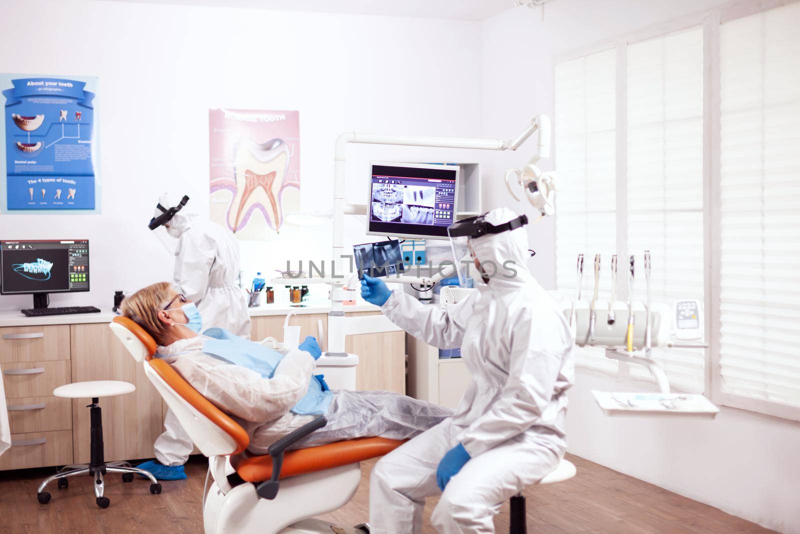 Dentist in protective gear agasint coroanvirus holding patient x-ray by DCStudio