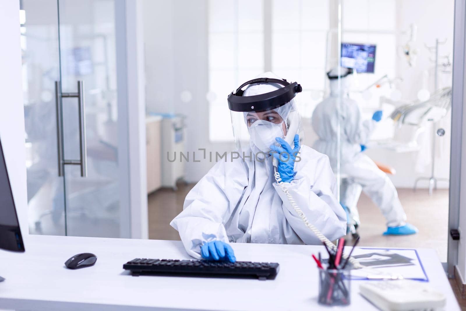 Dentist nurse in ppe suit discussing with patient on the phone by DCStudio