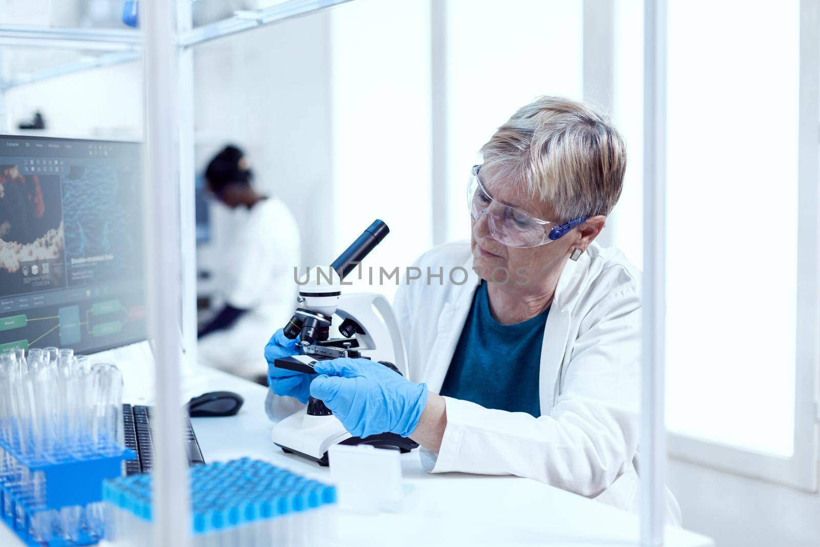 Senior scientist putting glass slide on microscope during medical investigation. Elderly researcher carrying out scientific research in a sterile lab using a modern technology.