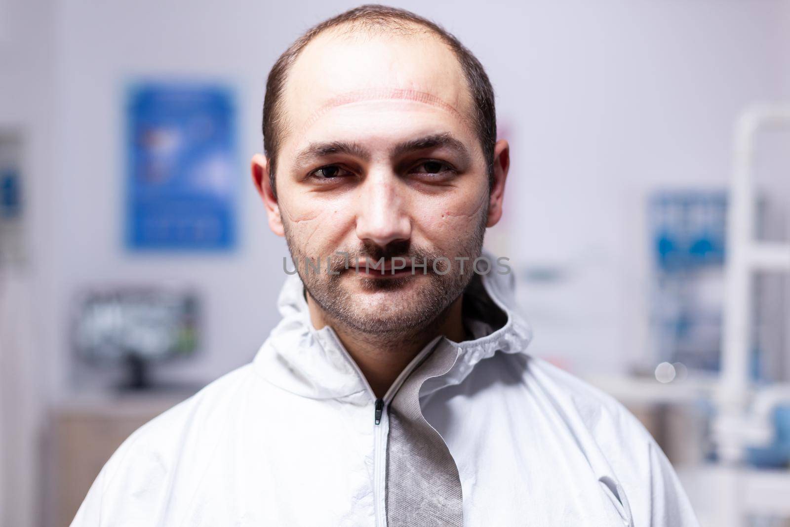 Close up of exhausted doctor in dental office looking on camera in the course of covid19 pandemic. Portrait of tired stomatologist wearing coronavirus ppe suit looking at camera.