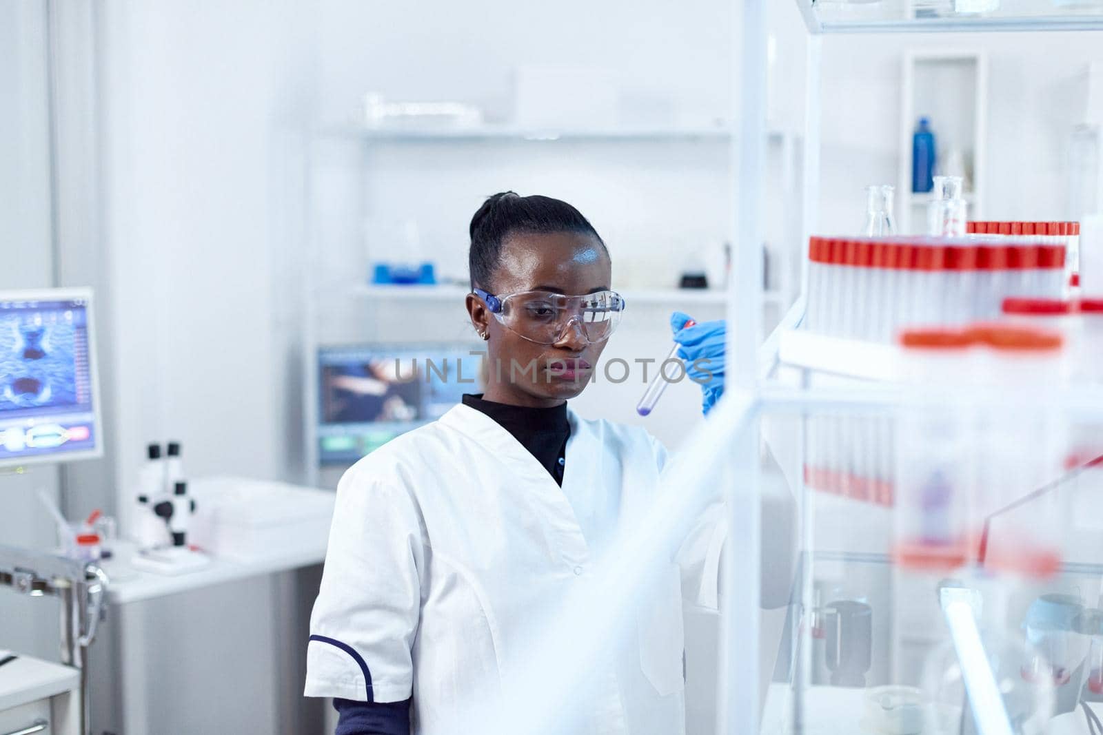 African scientist holding test tube with blue liquid for medical purpose. Black researcher in sterile laboratory conducting pharmacology experiment wearing coat.