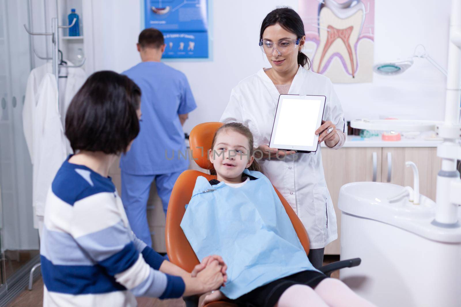 Dentistiry specialist talking about mouth hygine with young parent and kid. Stomatolog explaining teeth prevention to mother and child holding tablet pc with copy space available.