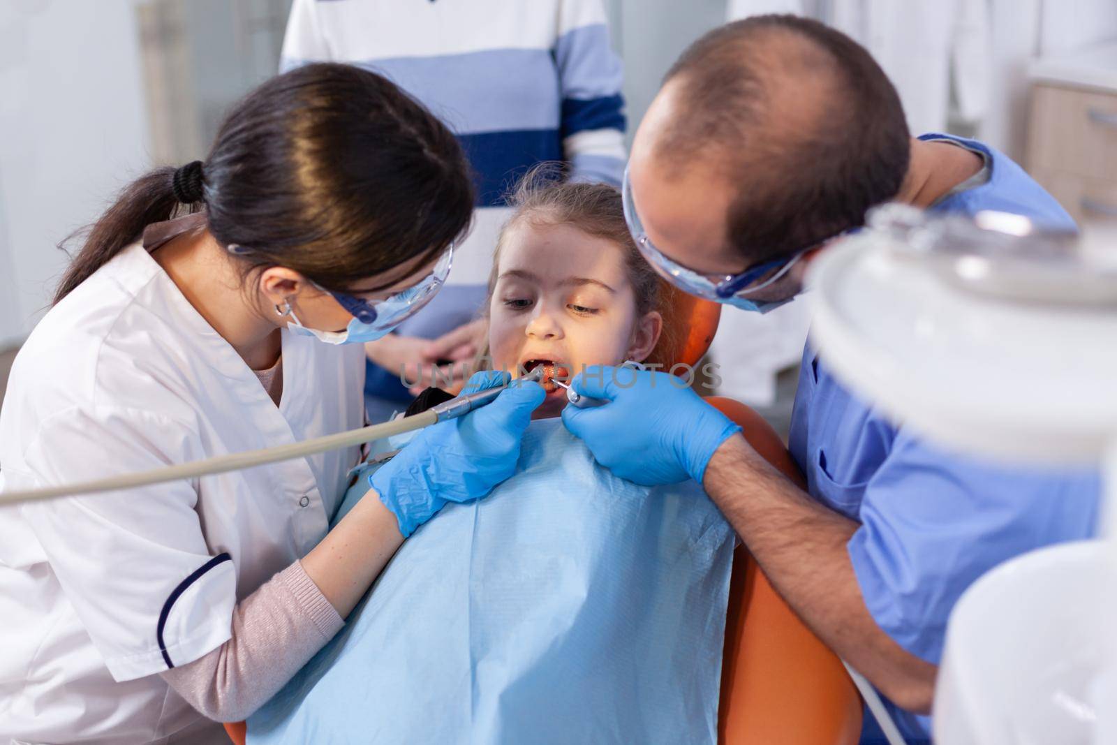 Dentist and assistant using instruments during dental treatment for little girl by DCStudio