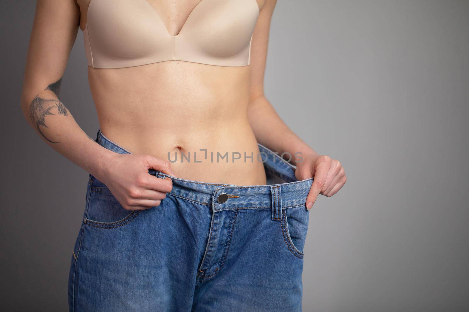 Young Woman Shows her Weight Loss and Wearing Her Old Jeans. Slim Girl in Big Jeans Showing How She Was Losing Weight When She Started Eating Healthy Food by uflypro