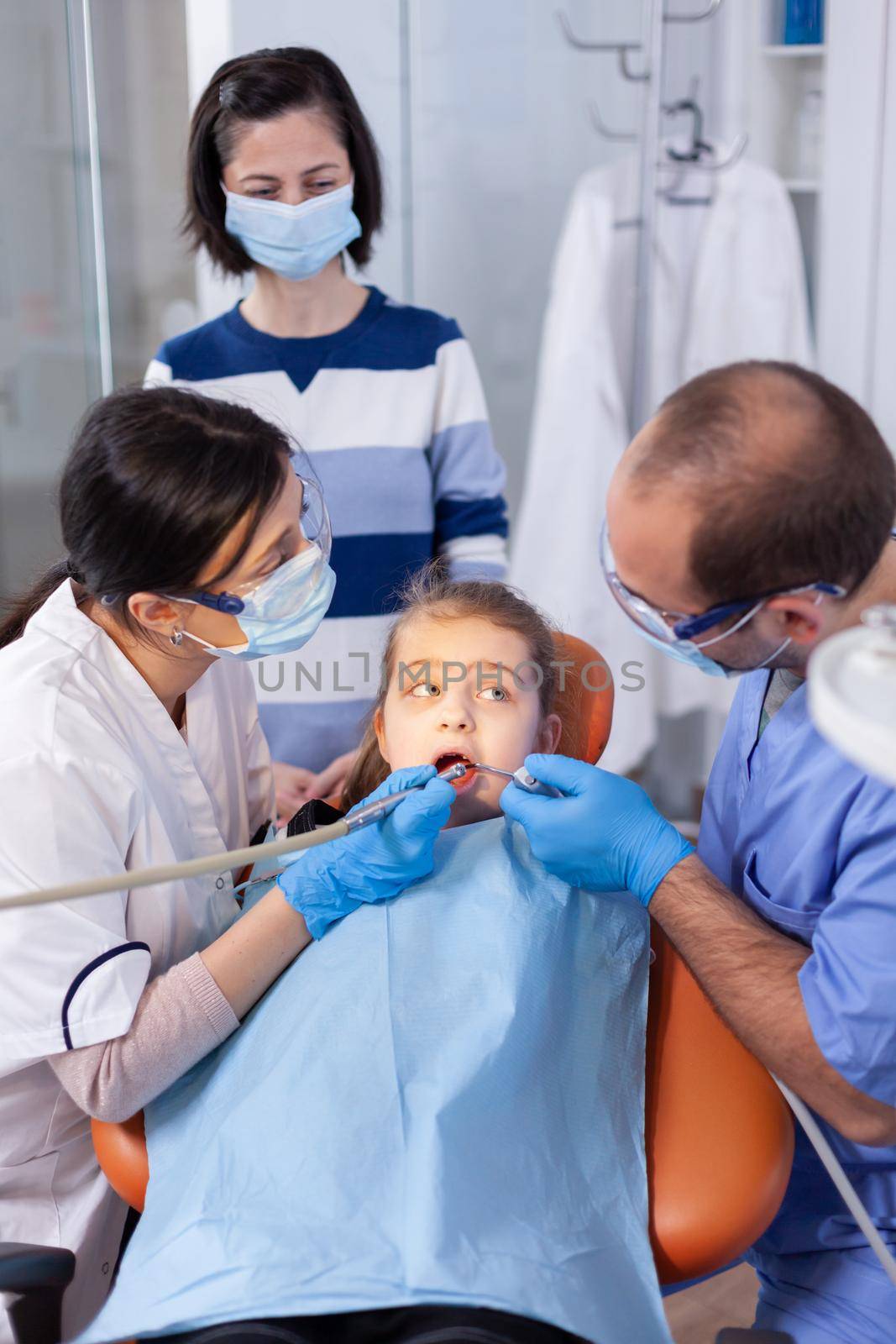 Child with mouth open looking at dentist assistant by DCStudio