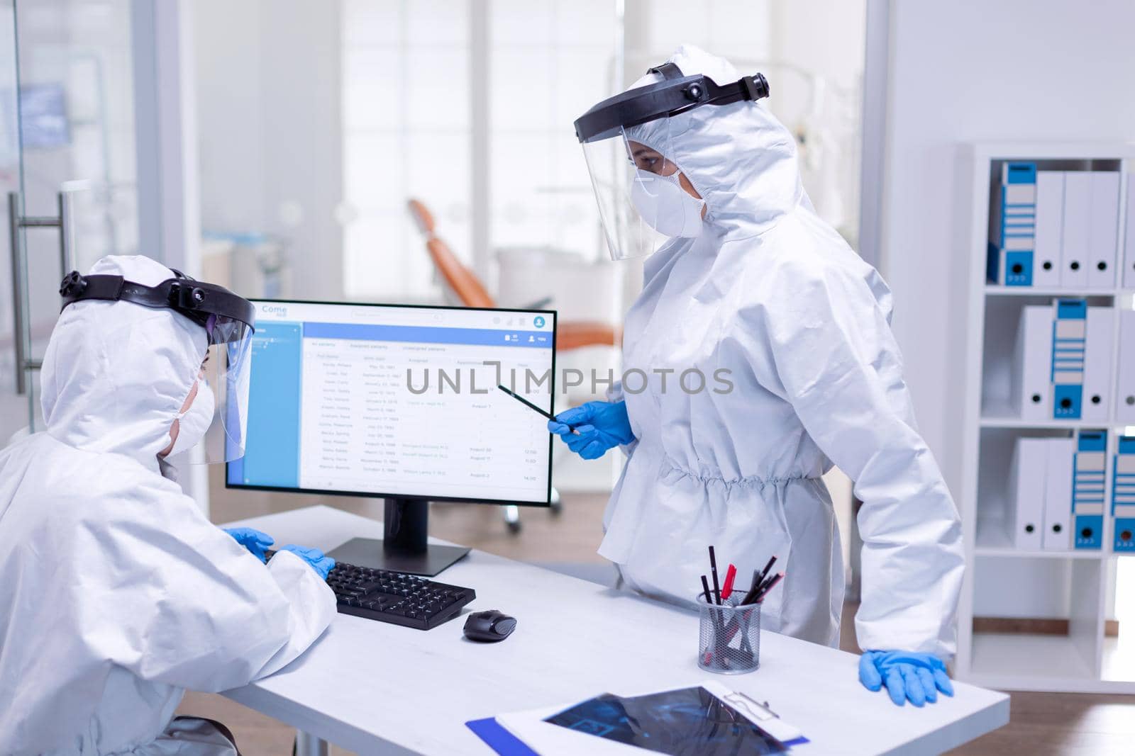 Dentist doctor wearing ppe suit talking with nurse at reception by DCStudio