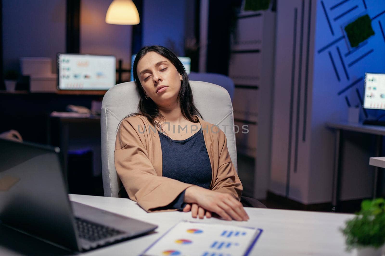 Overworked stressed woman sleeping laying chair back support in the course of deadline. Employee falling asleep while working late at night alone in the office for important company project.