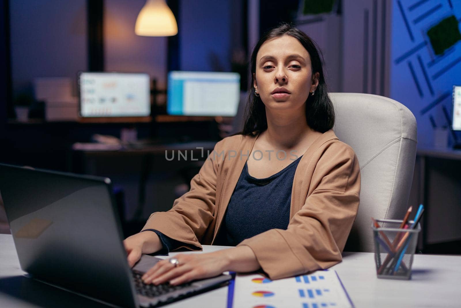 Businesswoman holding hands on laptop keyboard looking at camera. Smart woman sitting at her workplace in the course of late night hours doing her job.