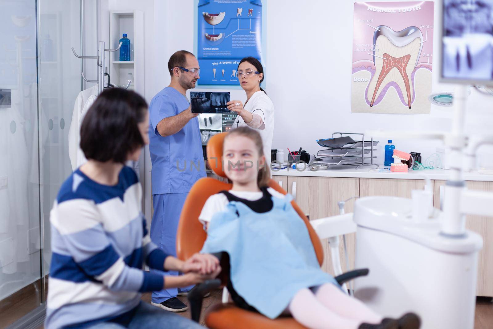 Dentist and assistant in dental office holding little girl jaw radiography by DCStudio