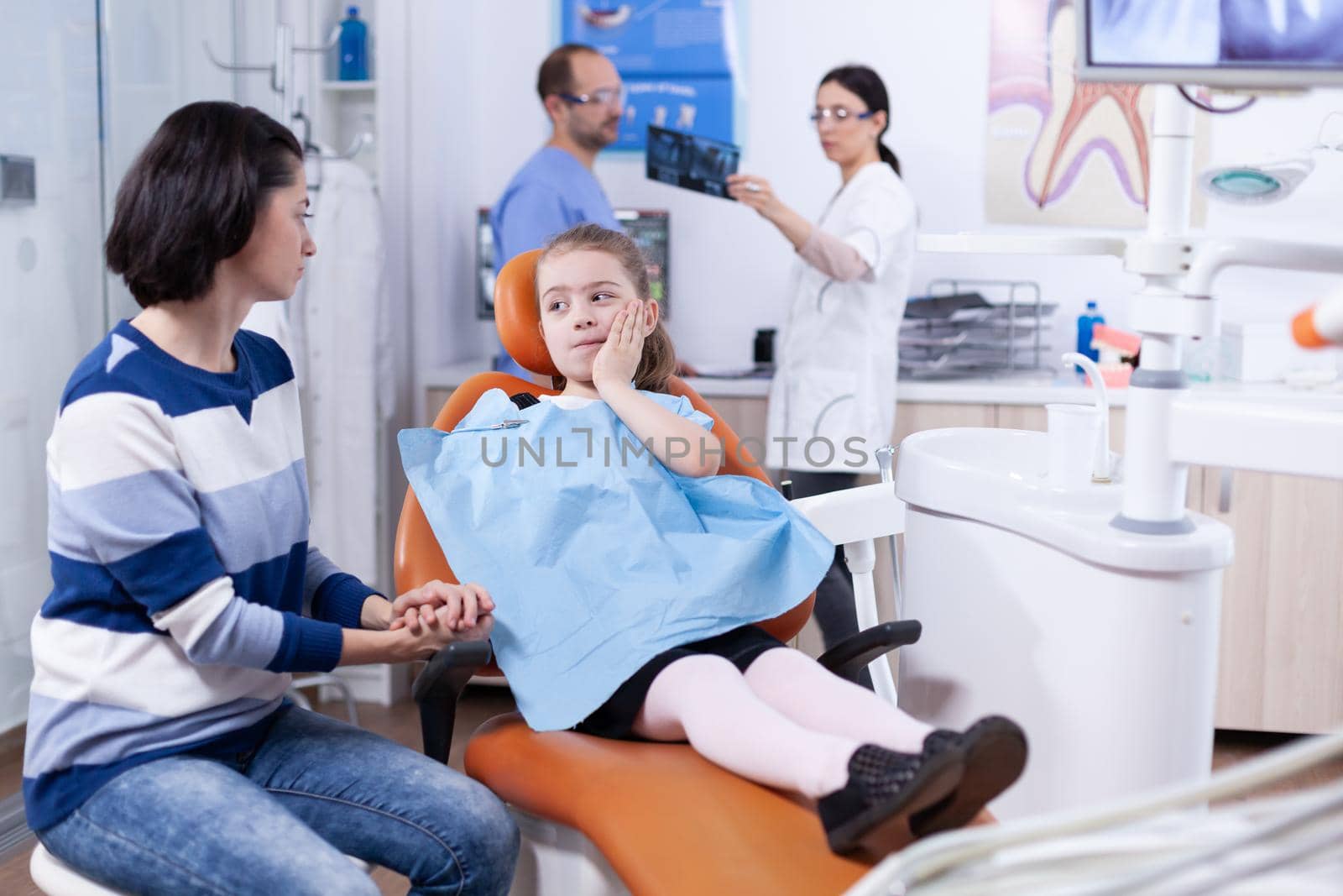 Little kid with painfull expression touching face during professional dental treatment by DCStudio