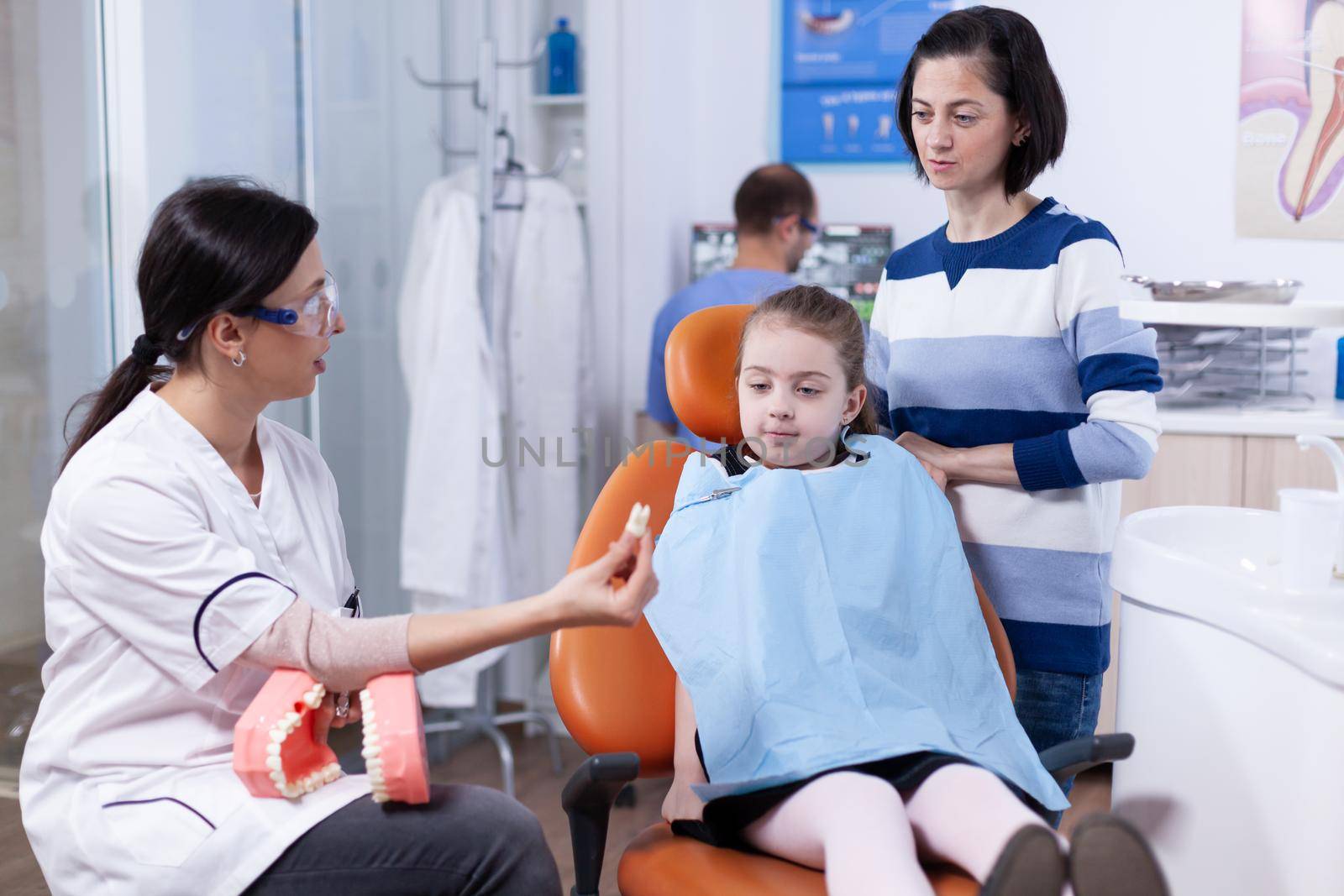 Orthodontist showing kid and her mother sample of teeth by DCStudio