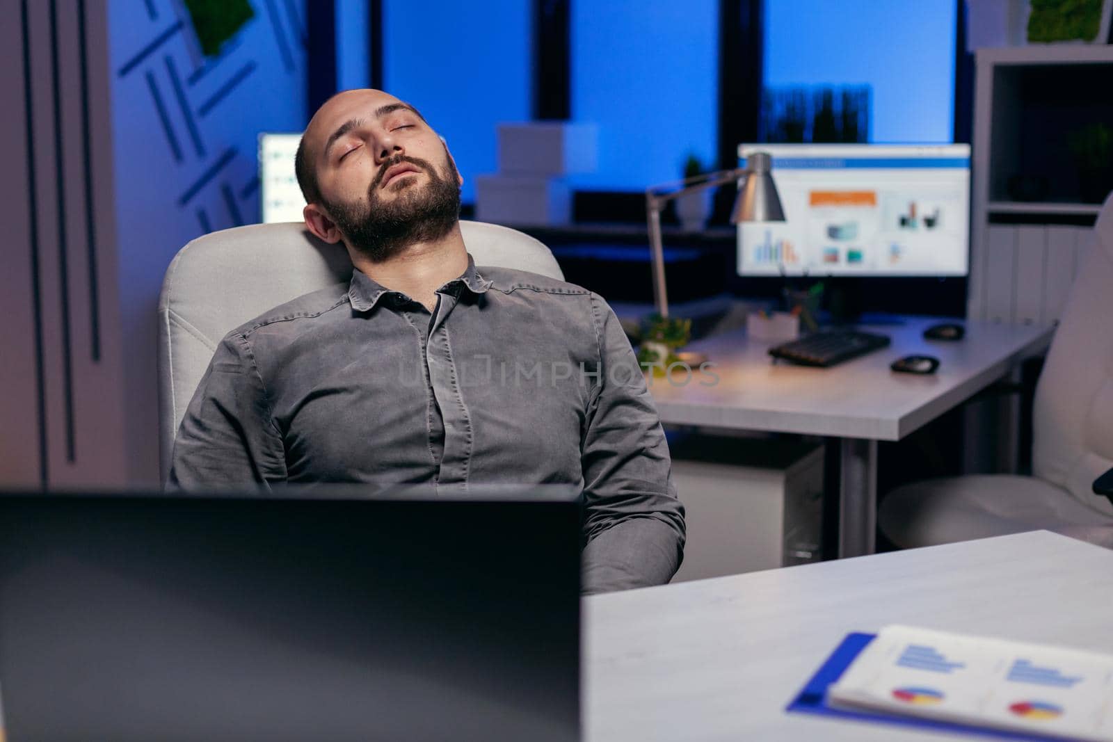 Exhausted hardworking businessman sleeping on chair. Workaholic employee falling asleep because of working late at night alone in the office for important company project.