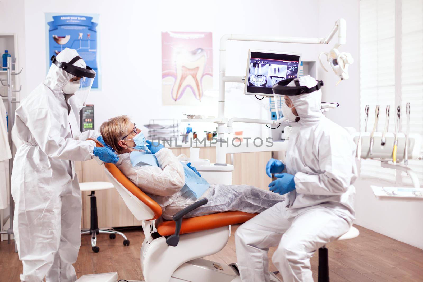 Dentist wearing equipment agasint coronavirus dicussing about teeth hygiene with senior patient. Elderly woman in protective uniform during medical examination in dental clinic.
