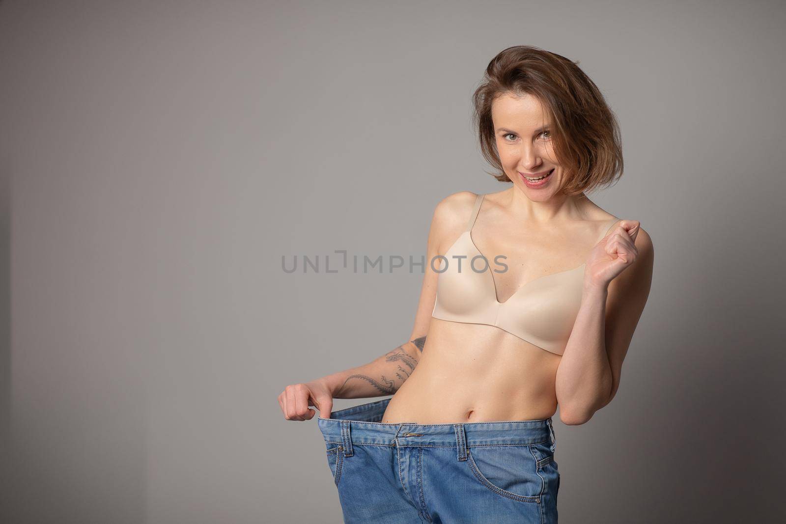 Young Woman Shows her Weight Loss and Wearing Her Old Jeans. Slim Girl in Big Jeans Showing How She Was Losing Weight. Woman with Perfect Fit Body. Weight Loss Concept. by uflypro