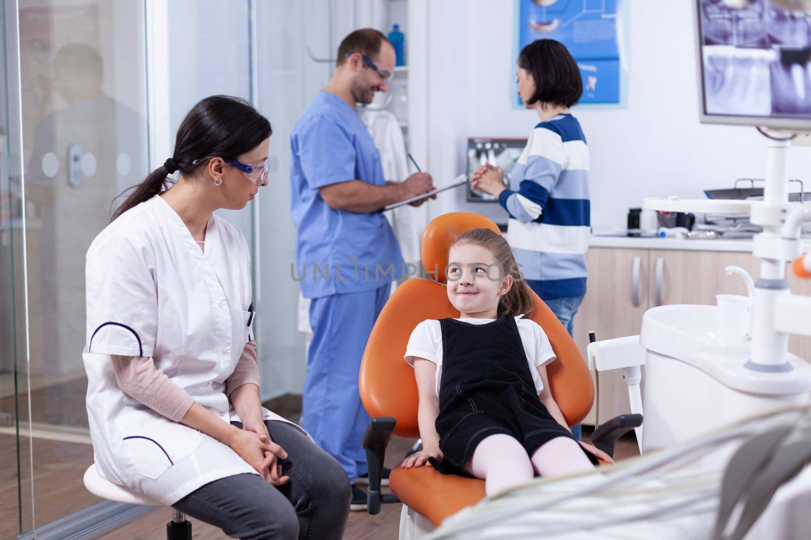 Little girl smiling at dentist sitting on chair waiting for teeth treatment by DCStudio