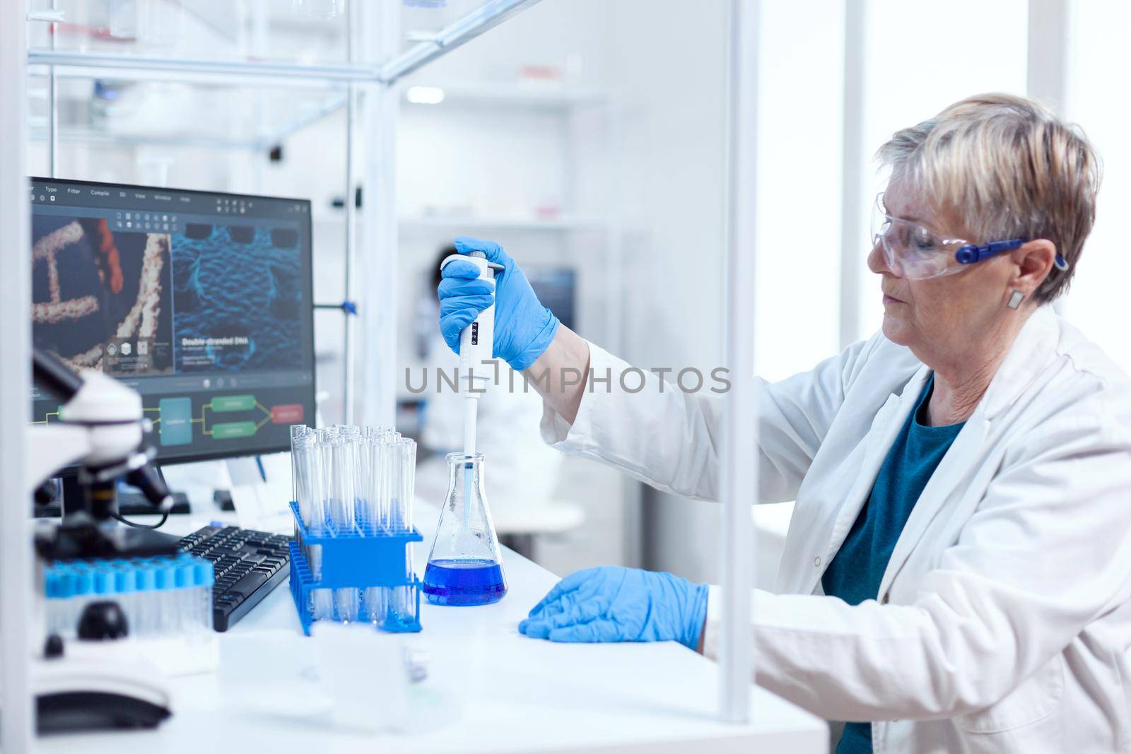 Senior scientist woman taking sample from glass flask using molecular pipette. People in innovative pharmaceutical laboratory with modern medical equipment for genetics research.