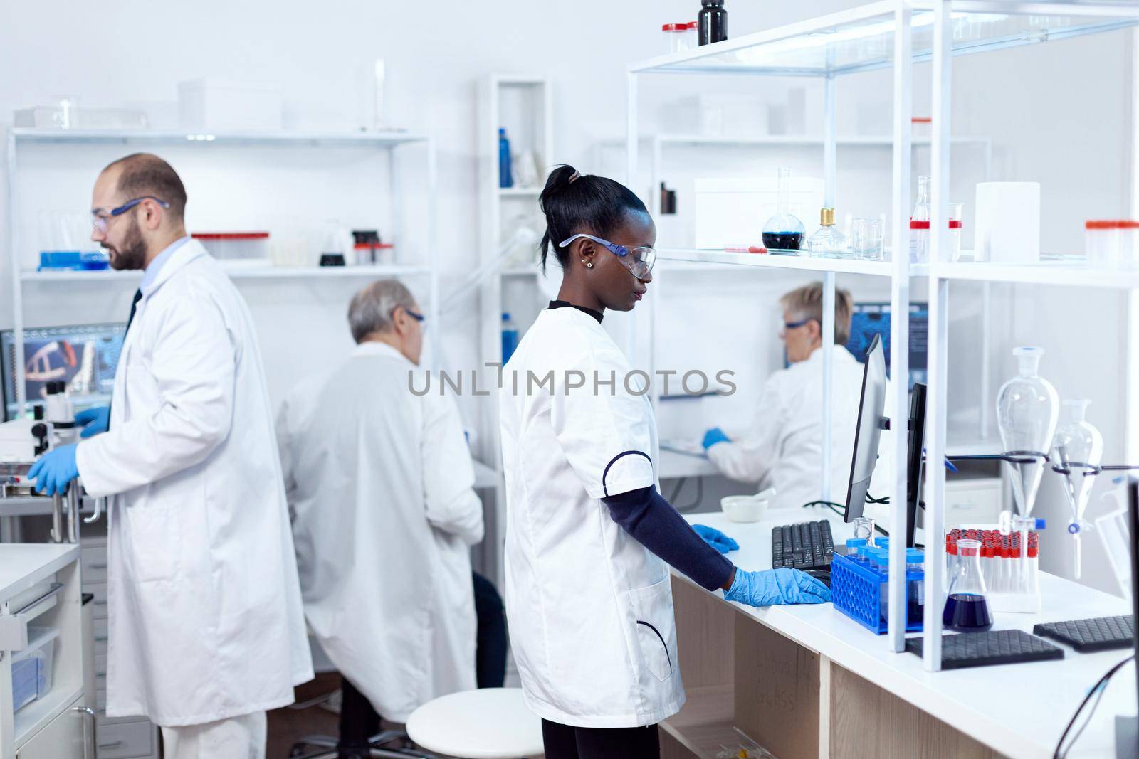 African scientist and her colleagues doing experiments in sterile laboratory. Multiethnic team of researchers working in microbiology lab testing solution for medical purpose.