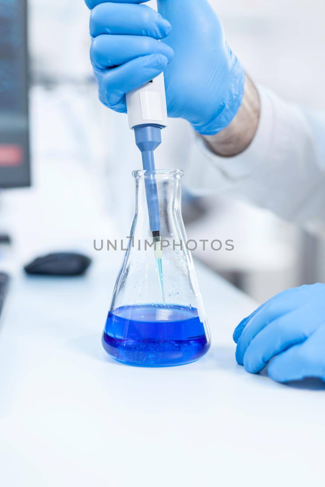 Scientist holding dispenser on test tubes in clinic pharmacy and medical research laboratory. Senior professional chemist using pippete with blue solution for microbiology tests.