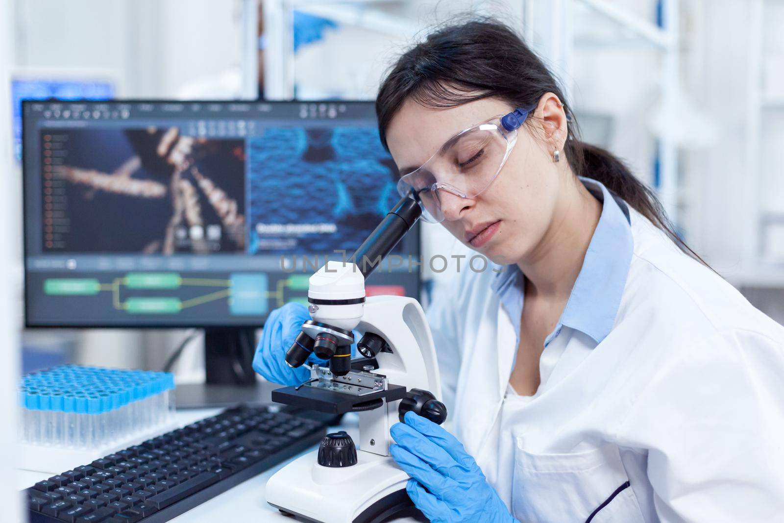 Female scientist in modern lab uses microscope for medicine vacine. Medical technician wearing white coat in sterile laboratory doing solution analysis.
