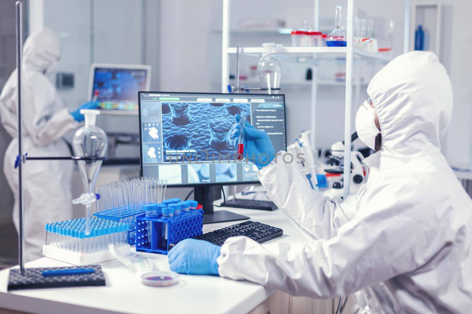 Scientist checking tube with blood analysis dressed in ppe by DCStudio