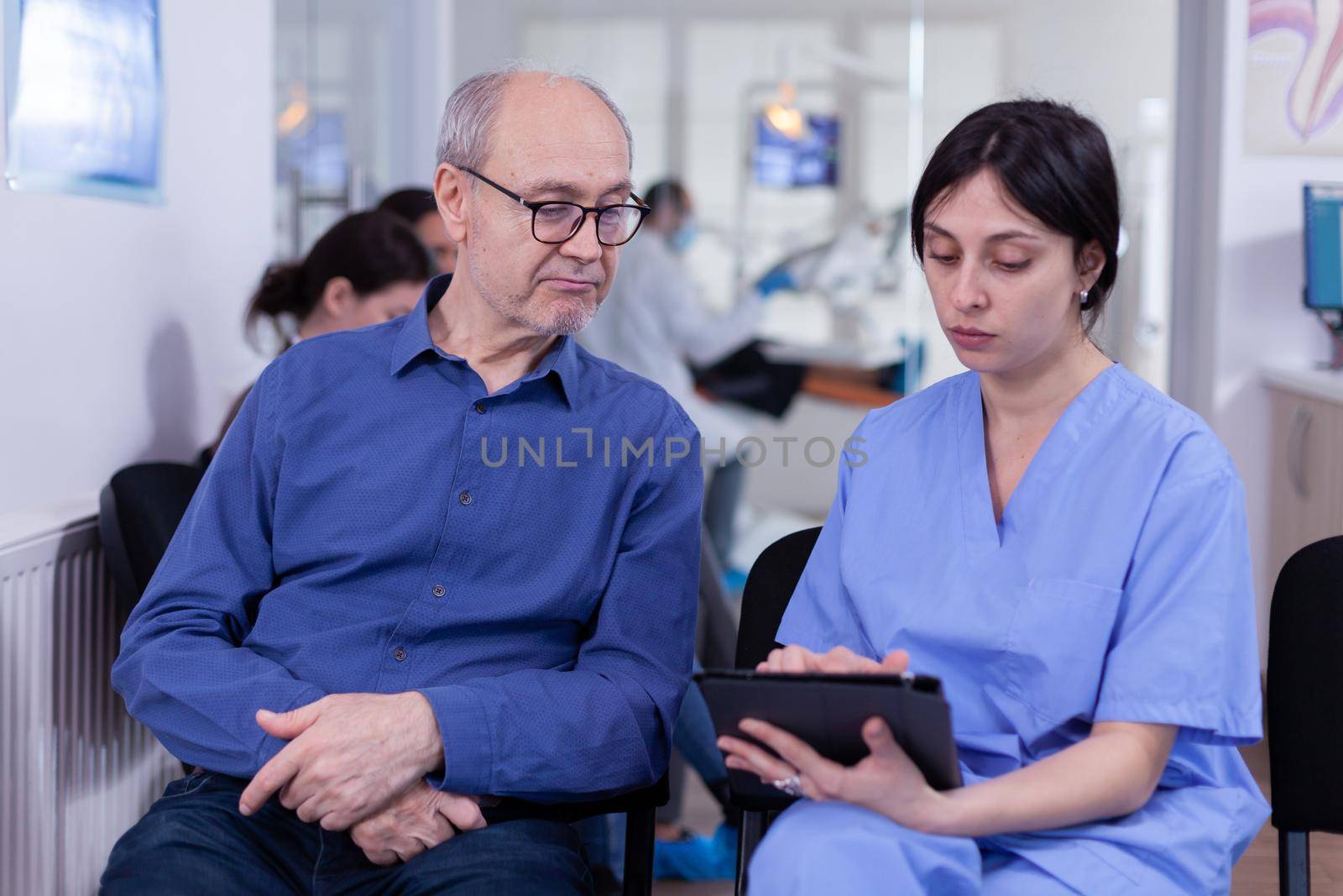 Nurse taking notes on tablet pc discussing with senior patient in dental office by DCStudio