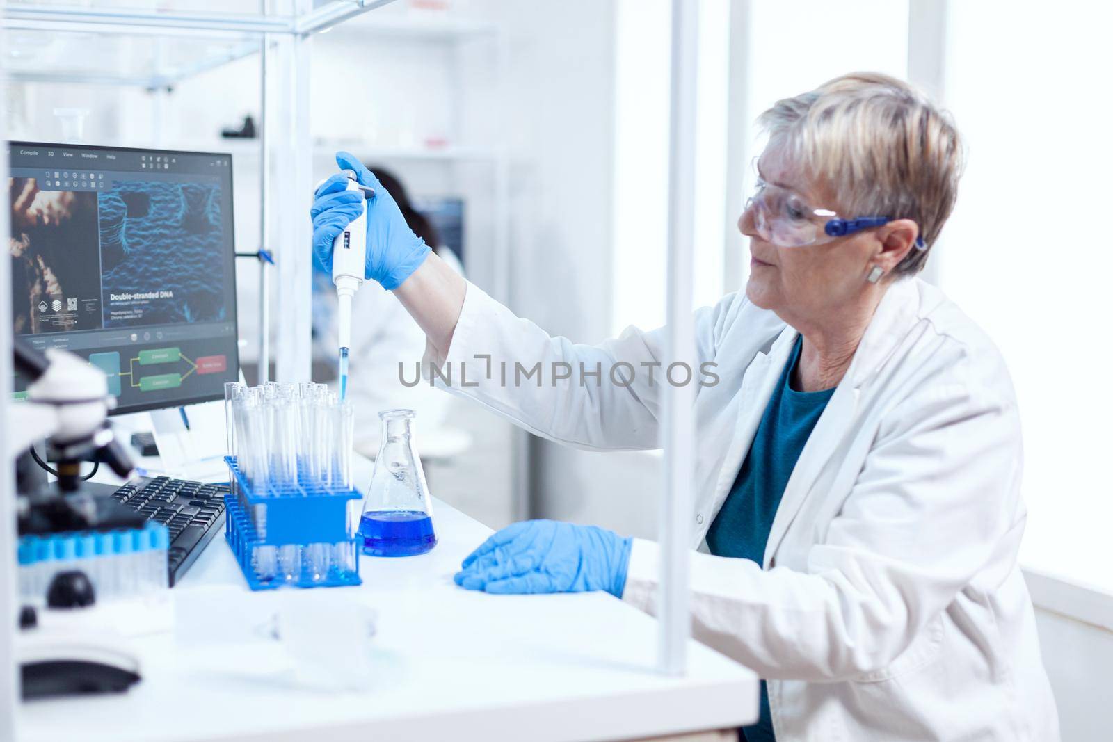 Senior scientist filling test tube wearing protective equipment using molecular dispenser. People in innovative pharmaceutical laboratory with modern medical equipment for genetics research.