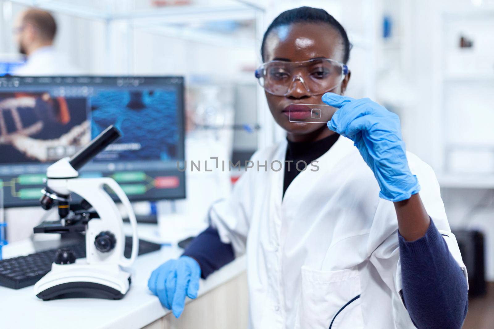Concentrated view of doctor african scientist holding glass microscope glass. Black healthcare scientist in biochemistry laboratory wearing sterile equipment.