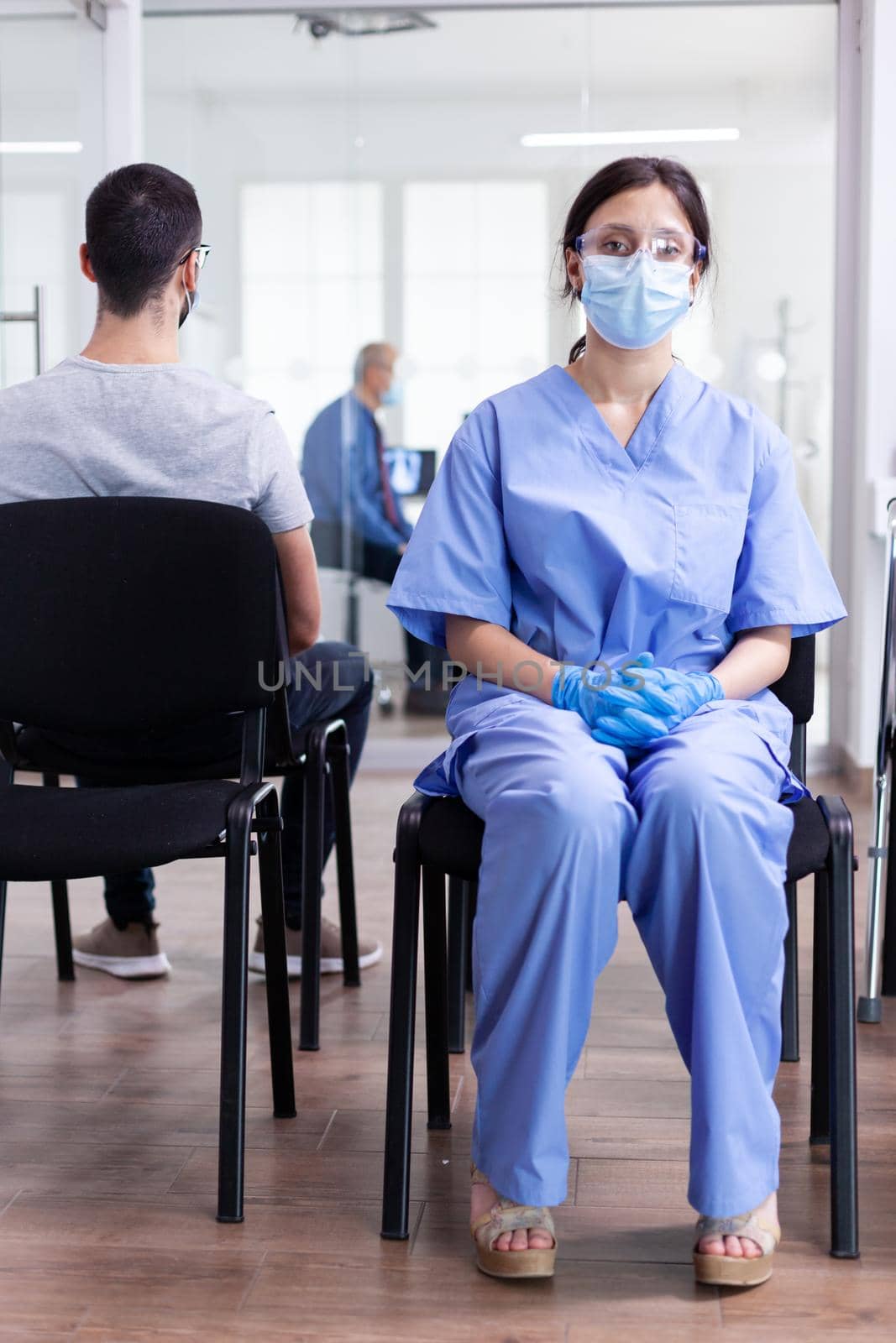 Exhausted assistant in hospital waiting room during global pandemic with coronavirus. Doctor consulting senior man in examination room. Physician, epidemic, care, surgical, corridor.