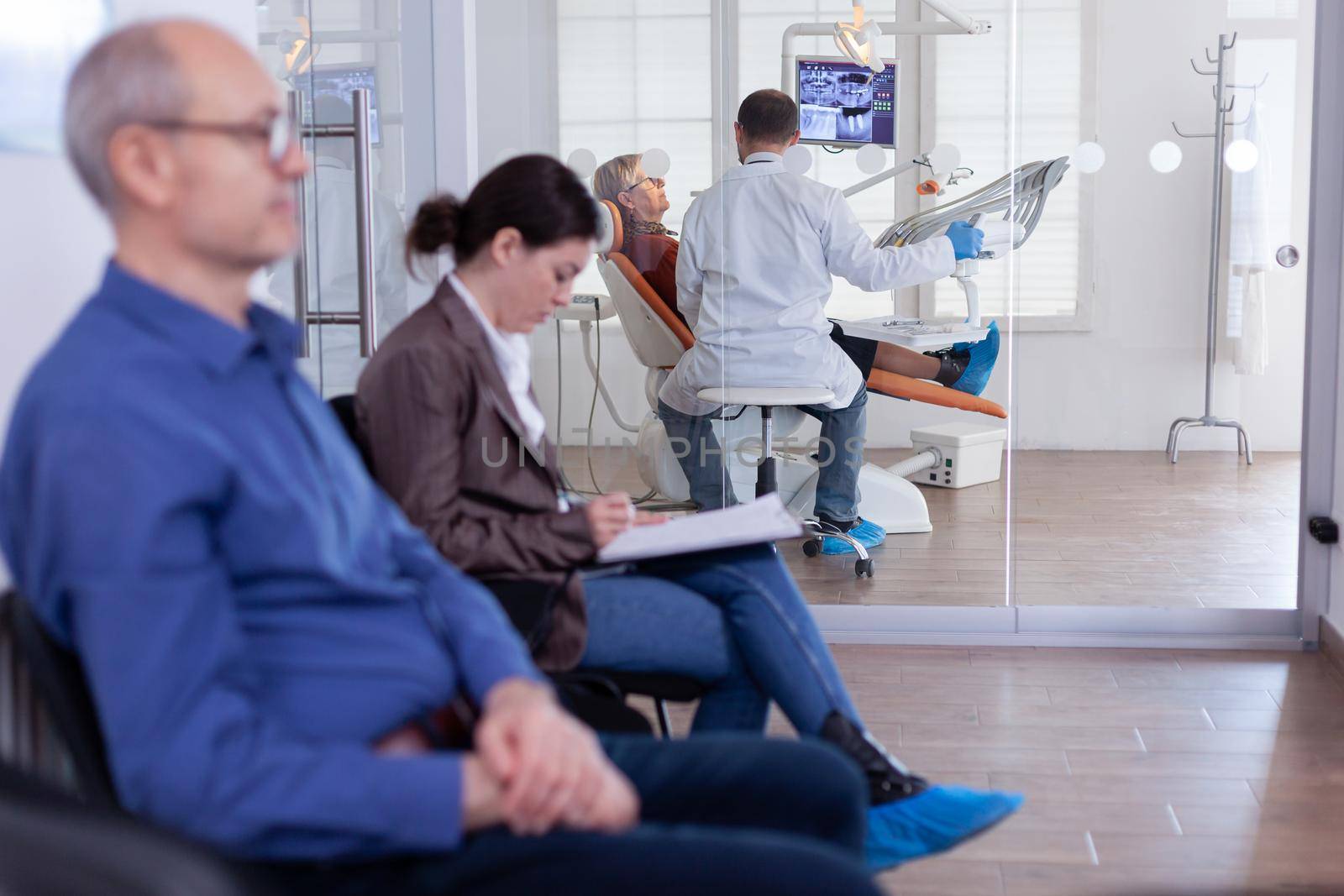 Senior woman sitting on chair in dental office listening dentist talking about diagnosis for teeth cavity looking at digital x-ray radiography. Patients filling form in waiting area.