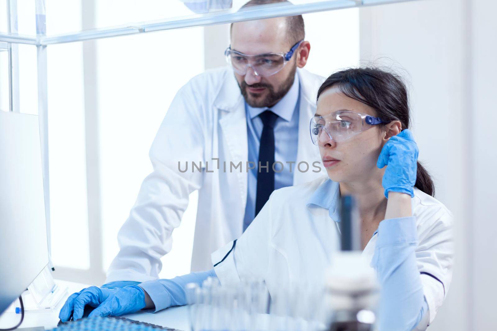 Male scientist helping assistant with genetic study wearing protective gear. Team of researchers doing pharmacology engineering in sterile laboratory for healthcare industry.