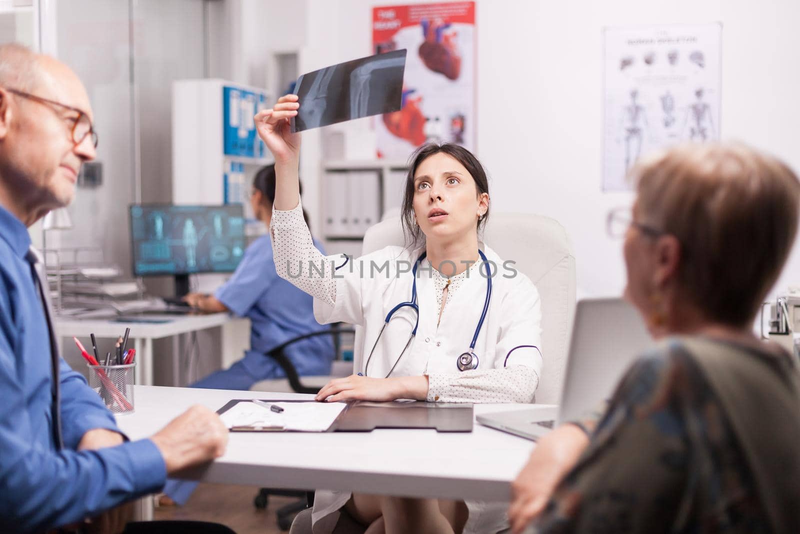Worried doctor examining x-ray of senior patient in hospital office. Pensioner couple during medical consultation. Medic wearing white coat and stethoscope.