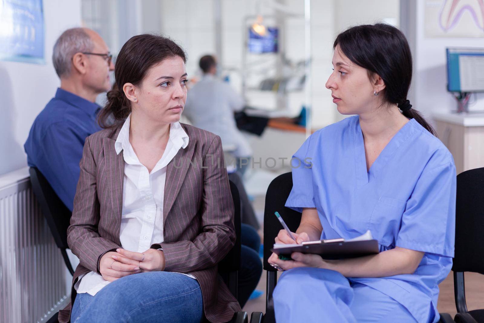Nurse taking notes on clipboard discussing with patient in dental clinic by DCStudio