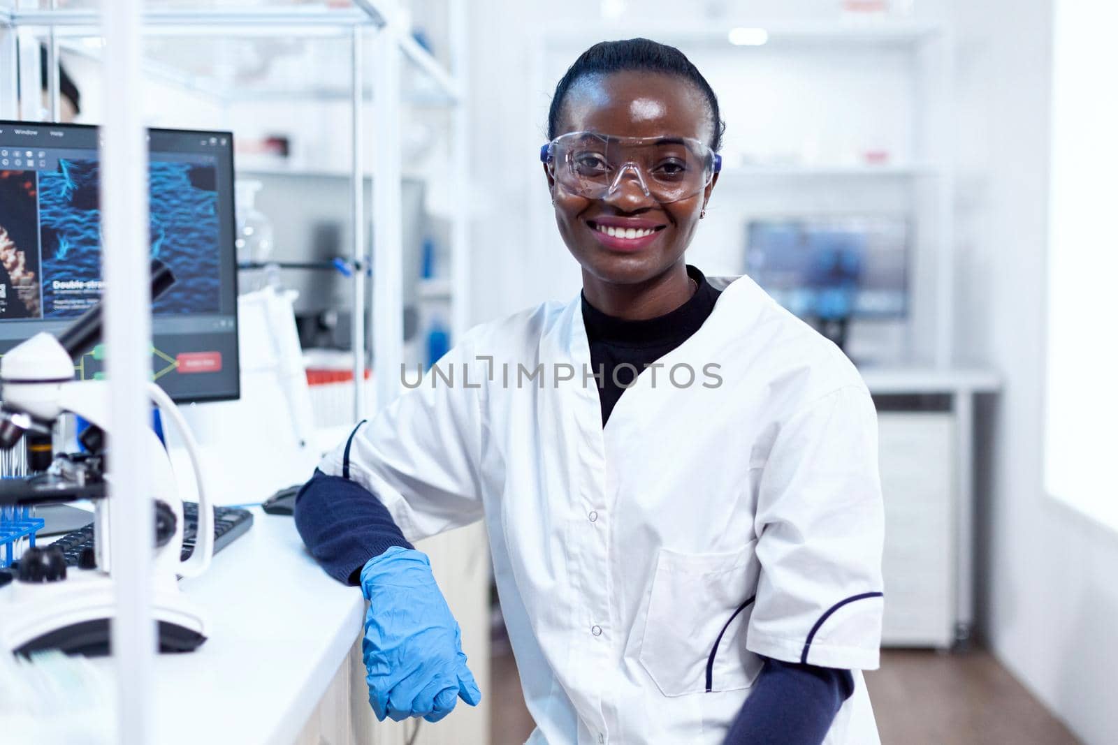 Portrait of professional african scientist smiling at camera in sterile laboratory. Multiethnic team of researchers working in microbiology lab testing solution for medical purpose.