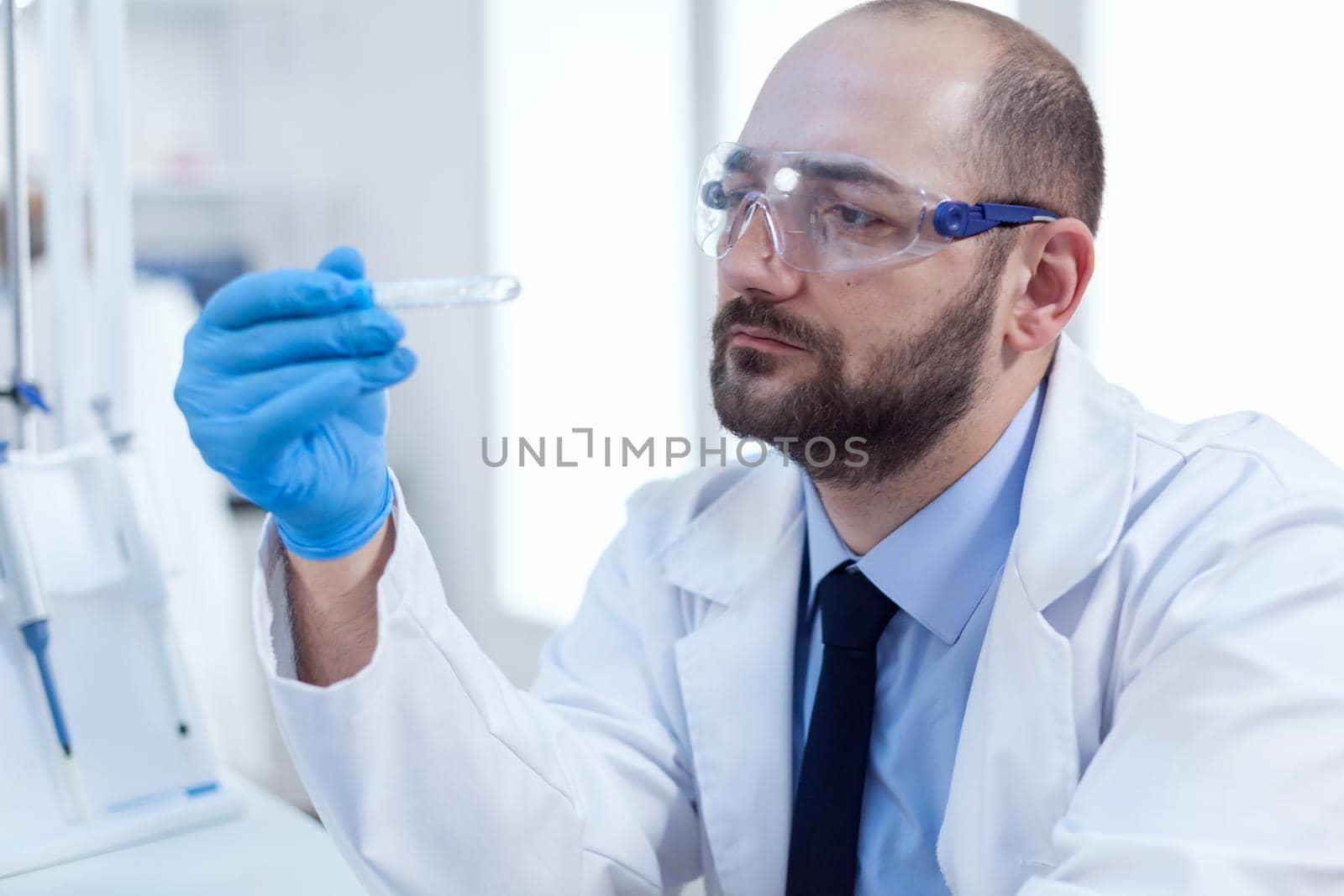 Chemist scientist holds test tube of glass in his hand for medicine experiment. Researcher in biotechnology sterile lab holding analysis in tube wearing gloves and protection glasses.