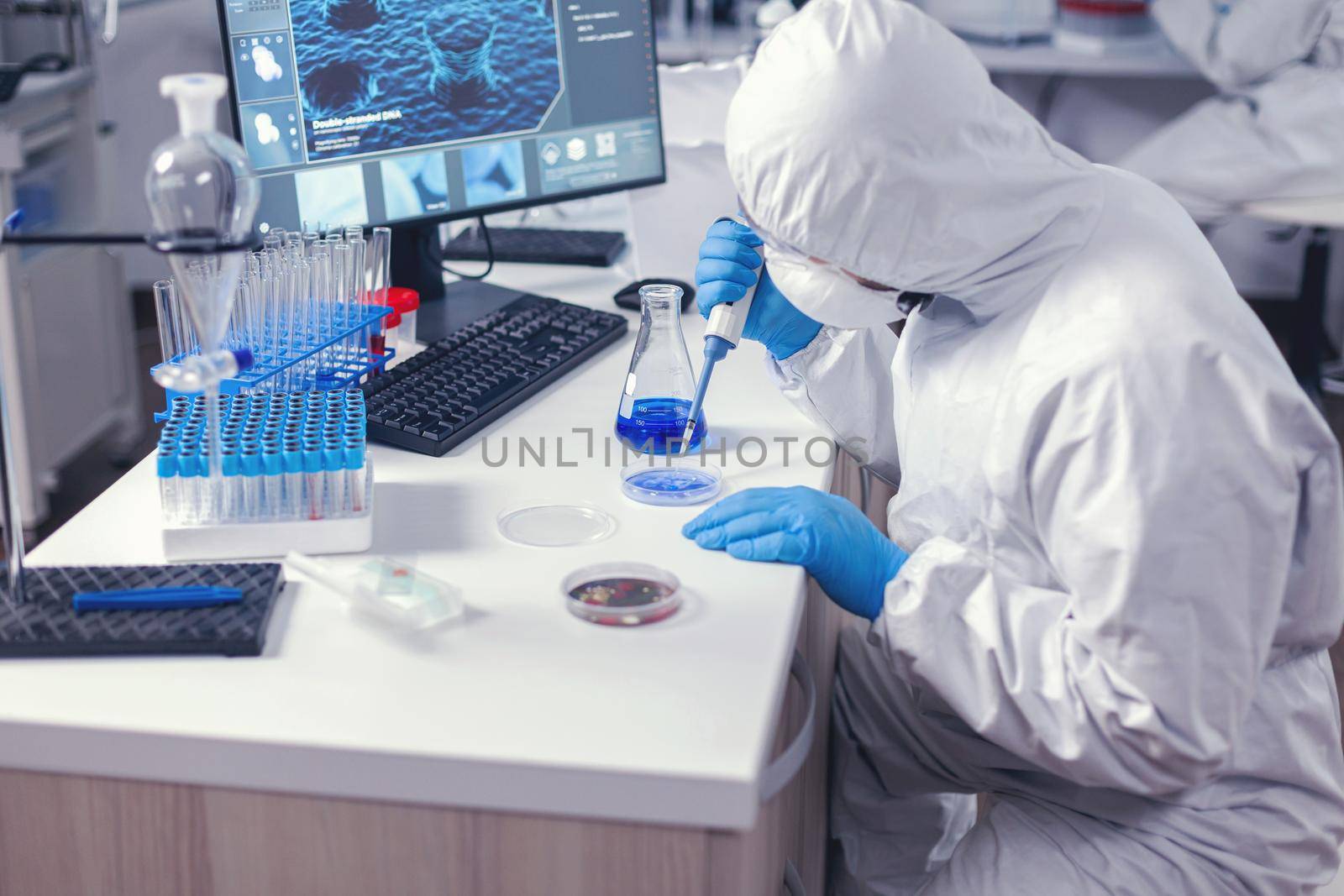 Focused lab technician pipetting solution into petri dish working on his workplace in modern lab. Chemist in modern laboratory doing research using dispenser during global epidemic with covid-19.