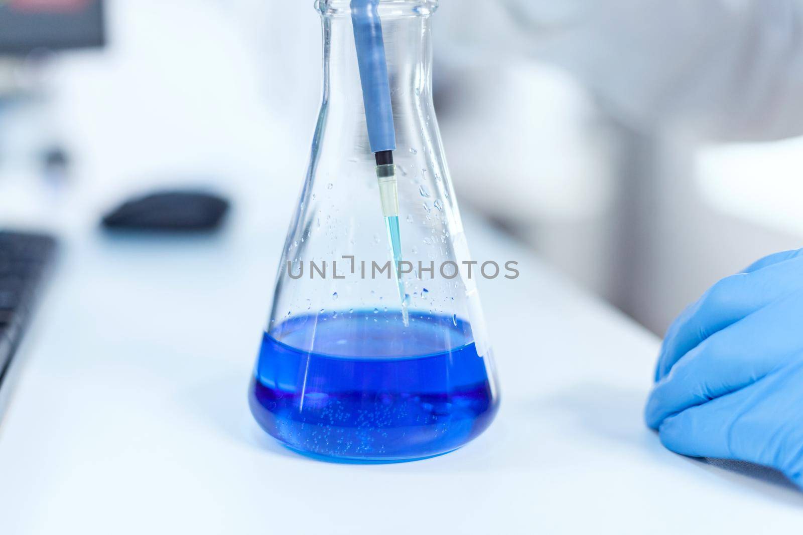 Employee of the scientific laboratory examining the liquid in a laboratory flask using dropper. Senior professional chemist using pippete with blue solution for microbiology tests.